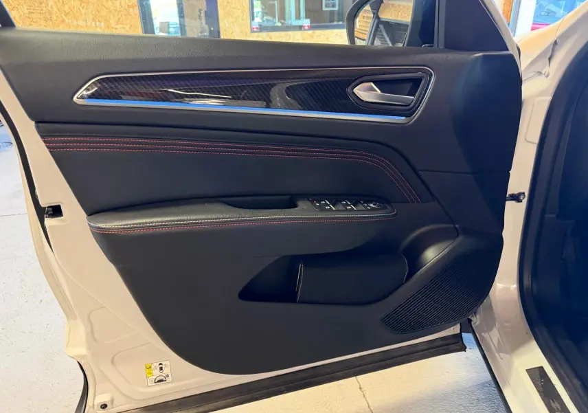 Vue rapprochée de la porte avant gauche blanche nacrée du Renault Arkana 1.6 E-Tech RS Line avec surpiqûres rouges et insert carbone.