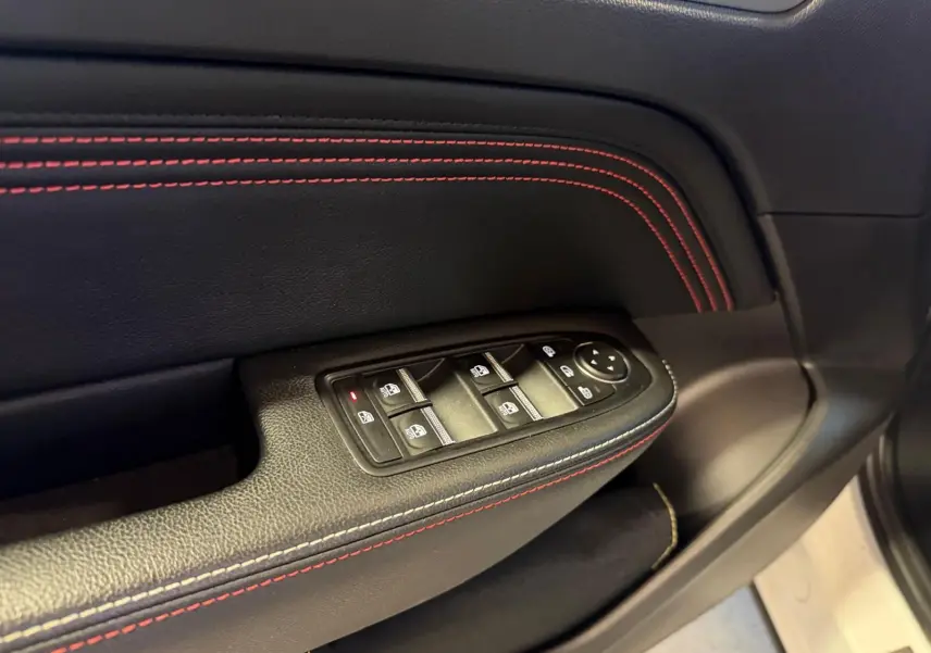 Gros plan sur la commande des vitres électriques côté gauche avec surpiqûres rouges sur garniture noire du Renault Arkana blanc nacré.