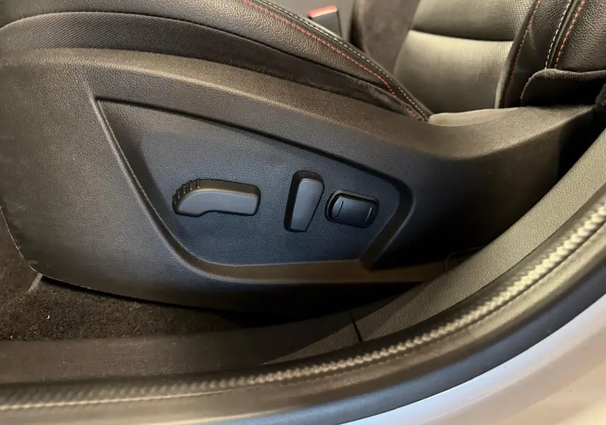 Gros plan sur les commandes électriques du siège conducteur noir avec surpiqûres rouges dans Renault Arkana blanc nacré.