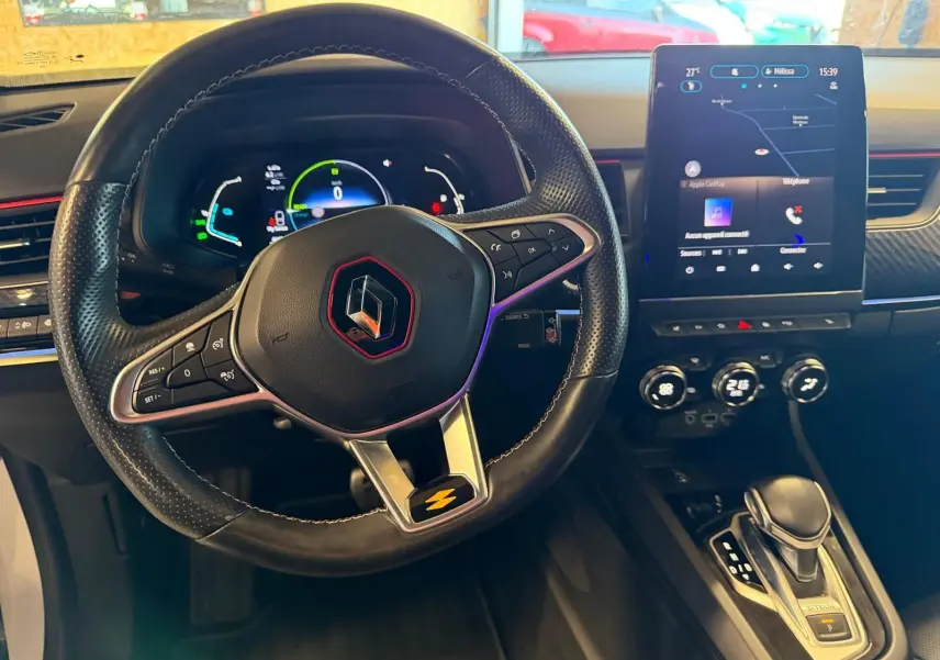 Vue intérieure centrée sur le volant noir avec logo Renault rouge, tableau de bord digital et écran tactile vertical.