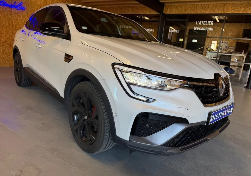 Renault Arkana blanc nacré en 3/4 avant droit, avec jantes noires et calandre noire brillante.