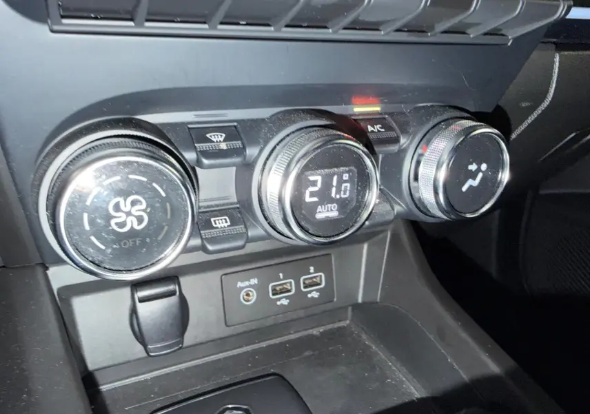 Gros plan sur la console centrale noire du Renault Arkana 1.6 E-Tech hybrid avec commandes de climatisation et ports USB visibles.