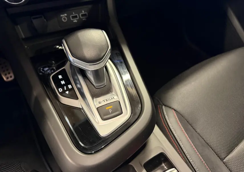 Gros plan sur le levier de vitesse automatique noir et argenté avec inscription E-TECH dans l’habitacle du Renault Arkana blanc nacré.