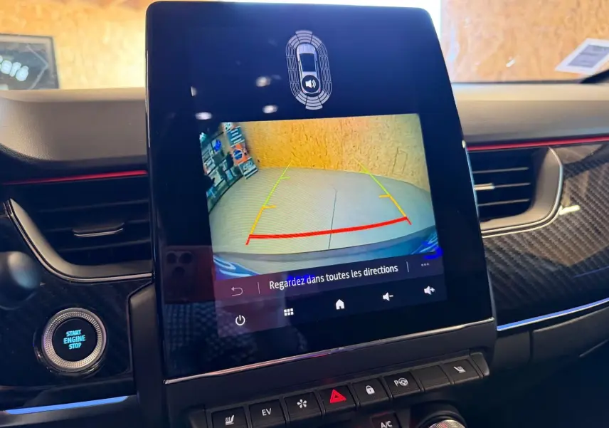 Écran tactile central montrant la caméra de recul, intérieur noir avec détails carbone et bande rouge sur tableau de bord.