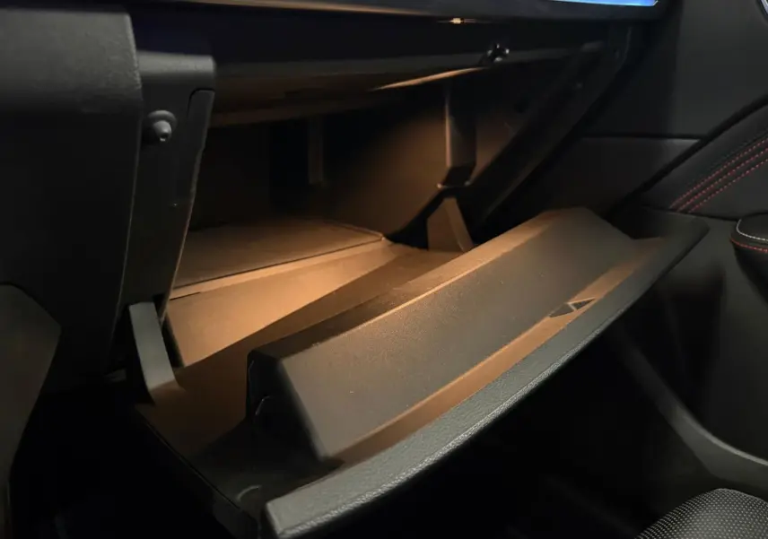 Gros plan sur la boîte à gants ouverte de la Renault Arkana 1.6 E-Tech blanc nacré, intérieur noir avec surpiqûres rouges.