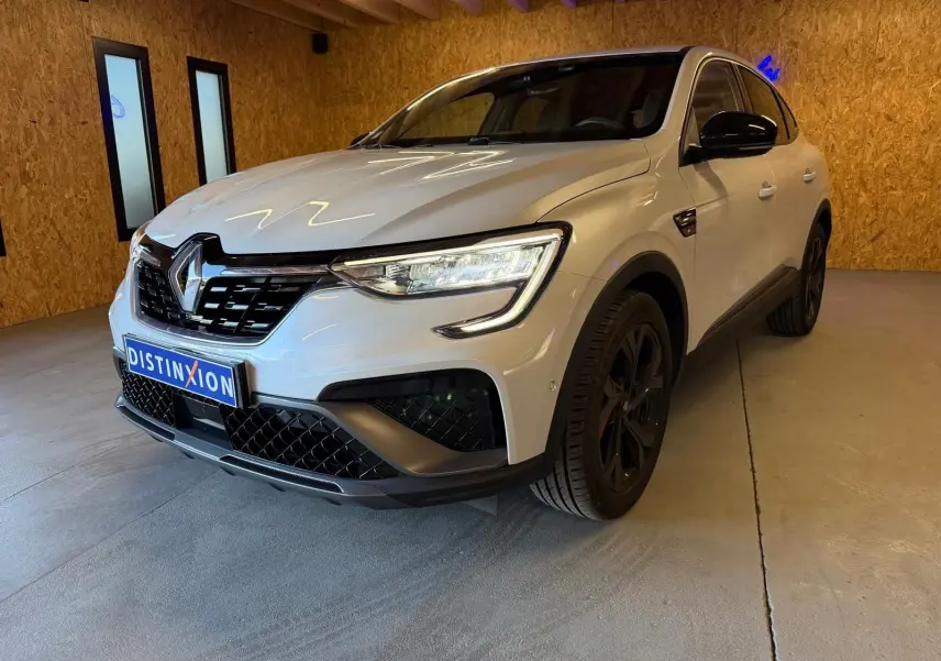 Renault Arkana blanc nacré en 3/4 avant droit, avec calandre noire et jantes alu noires, stationné en intérieur.