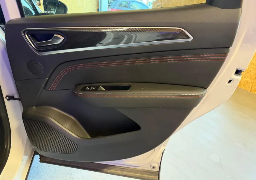 Vue intérieure de la porte arrière droite blanche nacrée du Renault Arkana 1.6 E-Tech avec surpiqûres rouges et insert carbone.