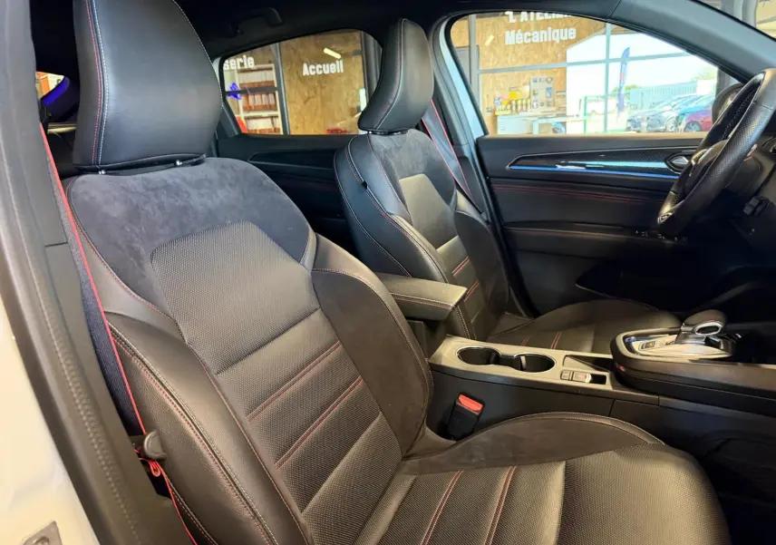 Vue intérieure côté conducteur de la Renault Arkana blanc nacré, sièges sport noirs avec surpiqûres rouges et console centrale.