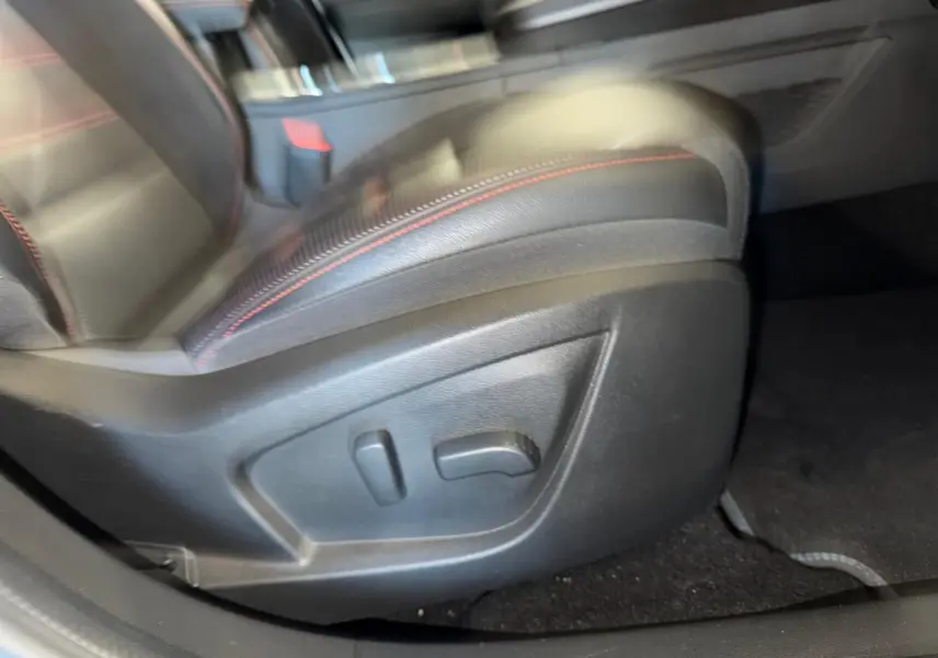 Gros plan sur le réglage électrique du siège conducteur en cuir noir avec surpiqûres rouges dans Renault Arkana blanc nacré.