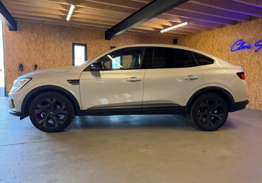 Renault Arkana blanc nacré en profil droit, jantes noires, avec toit incliné et détails RS Line visibles.
