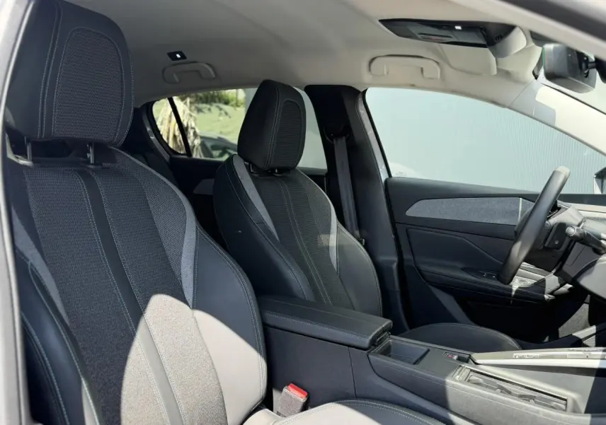 Vue intérieure côté conducteur de la Peugeot 308 Hybrid gris Artense, sièges tri matières avec surpiqûres bleues et accoudoir central.