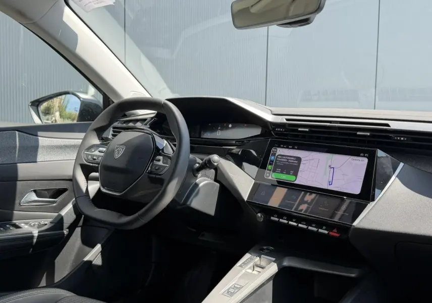 Vue intérieure côté conducteur de la Peugeot 308 Hybrid 2025 avec tableau de bord numérique et écran tactile de navigation.