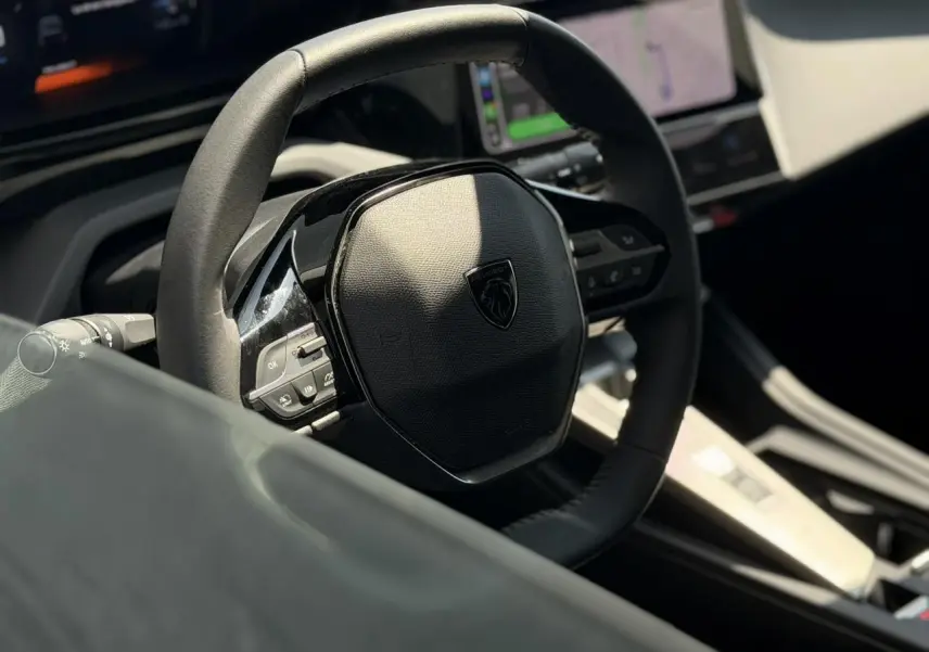 Intérieur de Peugeot 308 Hybrid 145, vue rapprochée du volant cuir noir avec commandes intégrées et tableau de bord digital.