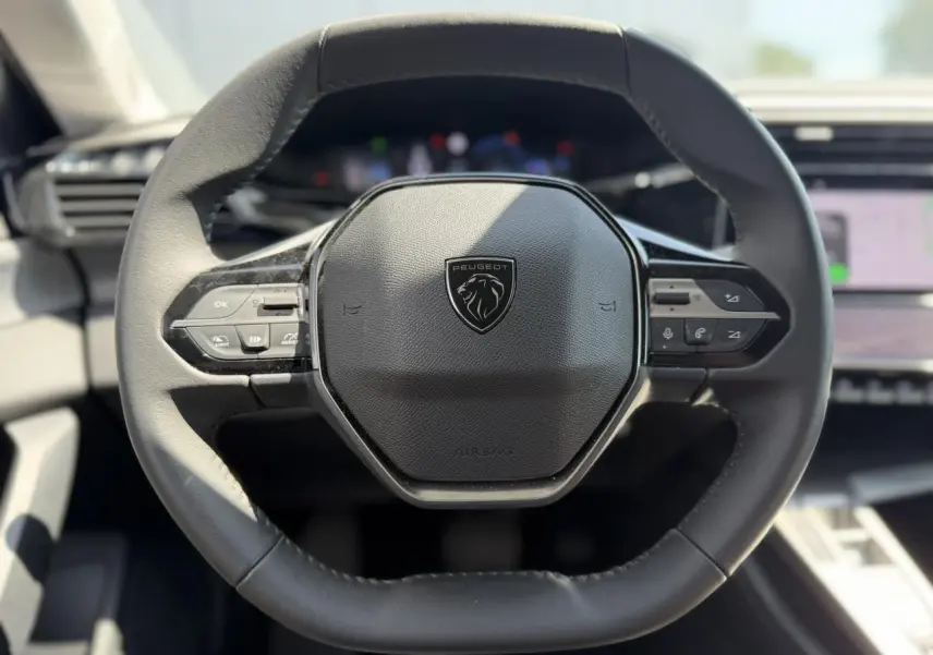 Volant cuir noir au design hexagonal du Peugeot 308 Hybrid 2025, avec commandes intégrées visibles de face.
