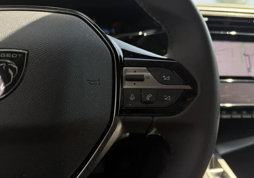 Gros plan sur le côté droit du volant cuir Peugeot 308 Hybrid 2025 avec commandes intégrées et écran tactile en arrière-plan.