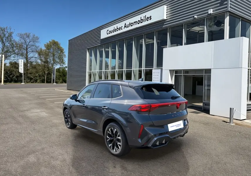 Vue 3/4 arrière droite d’un CUPRA TERRAMAR gris avec jantes 18’’ Atomic anthracites devant un concessionnaire.