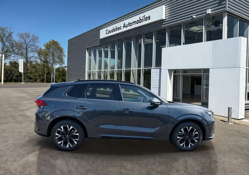 Vue latérale droite du CUPRA TERRAMAR gris 2025 avec jantes 18'' Atomic anthracites devant un concessionnaire.