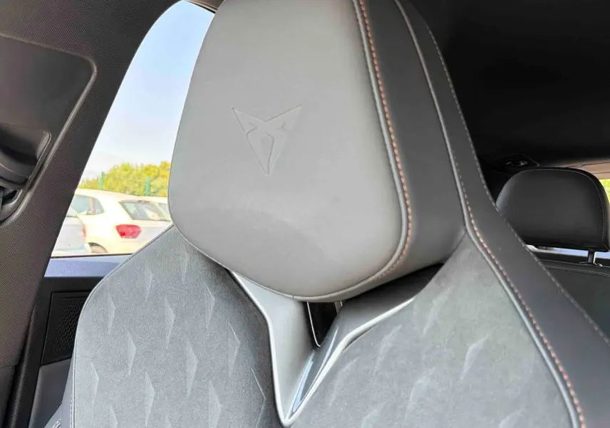 Gros plan sur l’appuie-tête avant gris avec logo Cupra embossé et surpiqûres marron à l’intérieur du CUPRA Terramar.