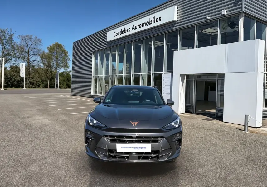 Vue avant d'une CUPRA TERRAMAR 1.5 eHybrid grise stationnée devant un showroom avec logo cuivré sur le capot.