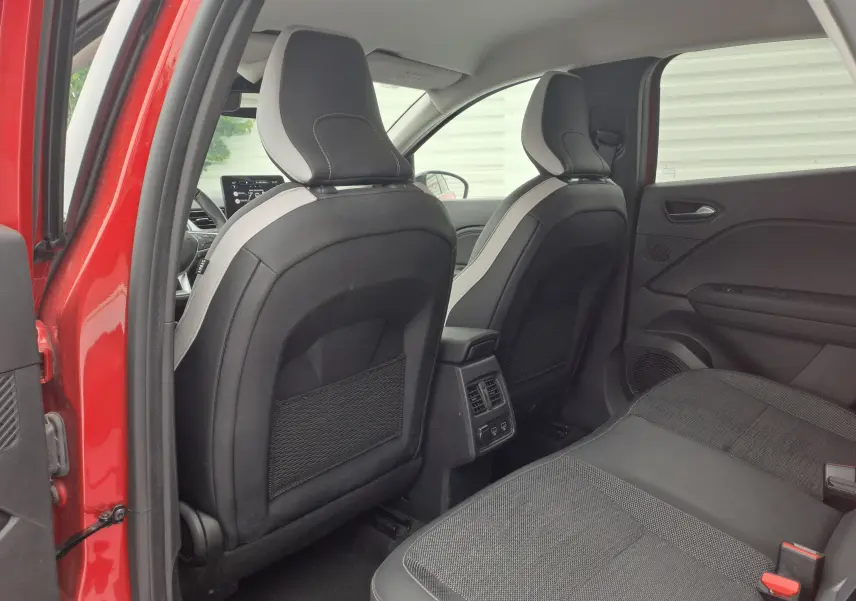 Intérieur arrière du Renault Captur TCE 90CH TECHNO 2024 rouge flamme, sièges noirs avec surpiqûres grises et console centrale avec prises USB.
