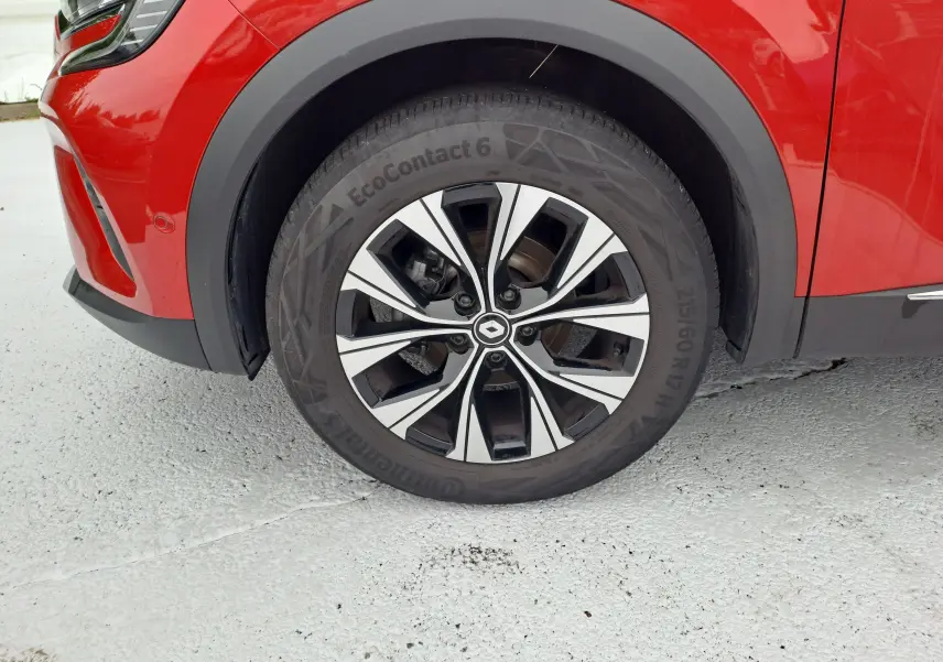 Gros plan sur la roue avant gauche du Renault Captur rouge flamme métal, mettant en valeur la jante alliage au design moderne.