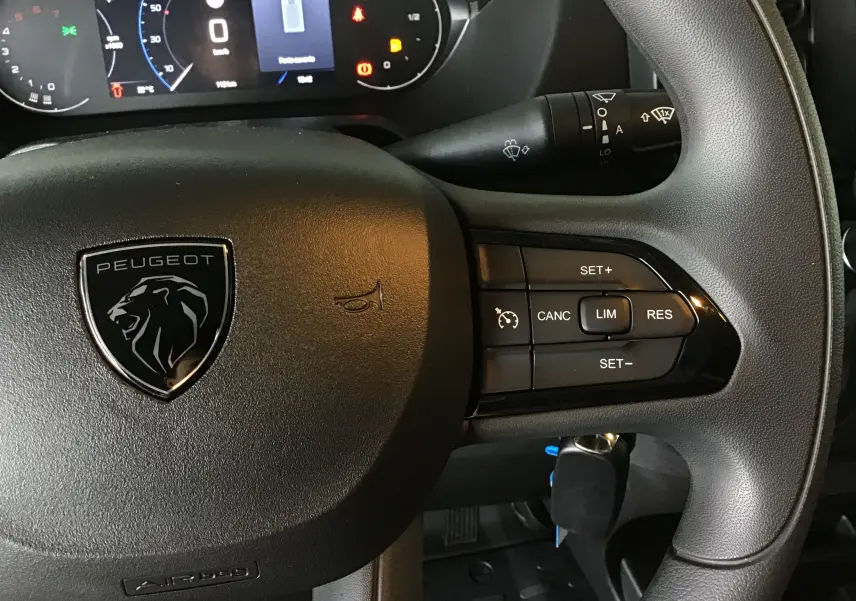 Gros plan sur le volant noir du Peugeot Boxer Fourgon 2025 avec commandes de régulateur et logo lion central.