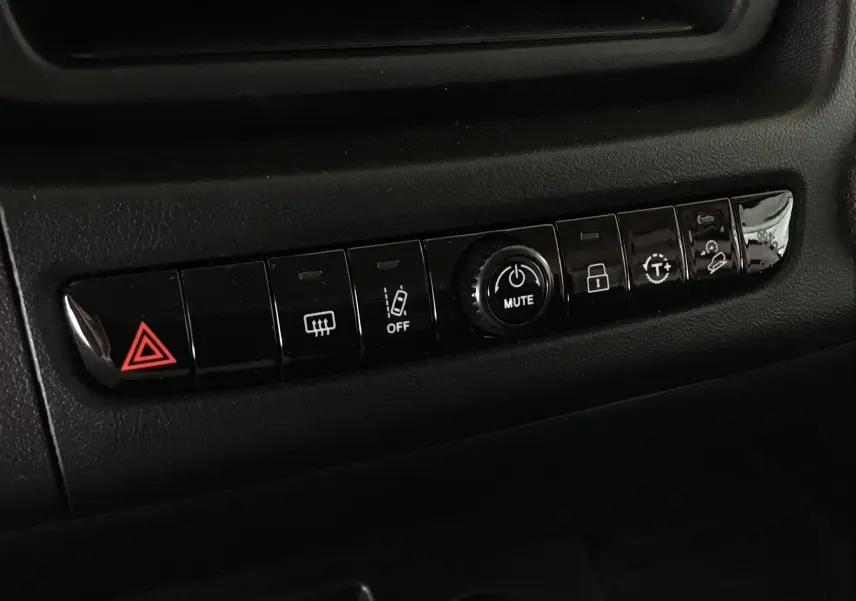 Gros plan sur la rangée de boutons de commande noirs avec symbole d'alerte rouge dans l'habitacle du Peugeot Boxer Fourgon blanc.