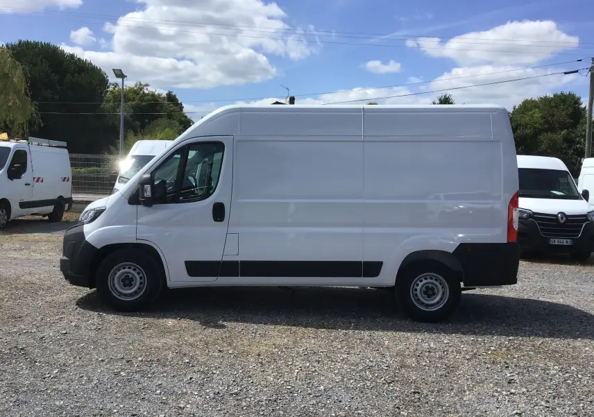 Profil côté gauche d’un fourgon blanc Peugeot Boxer L2H2 2025 avec protections noires sur un sol gravillonné.