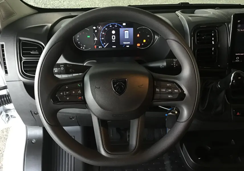 Vue centrée sur le volant noir du Peugeot Boxer Fourgon 2025 avec tableau de bord numérique et commandes intégrées.