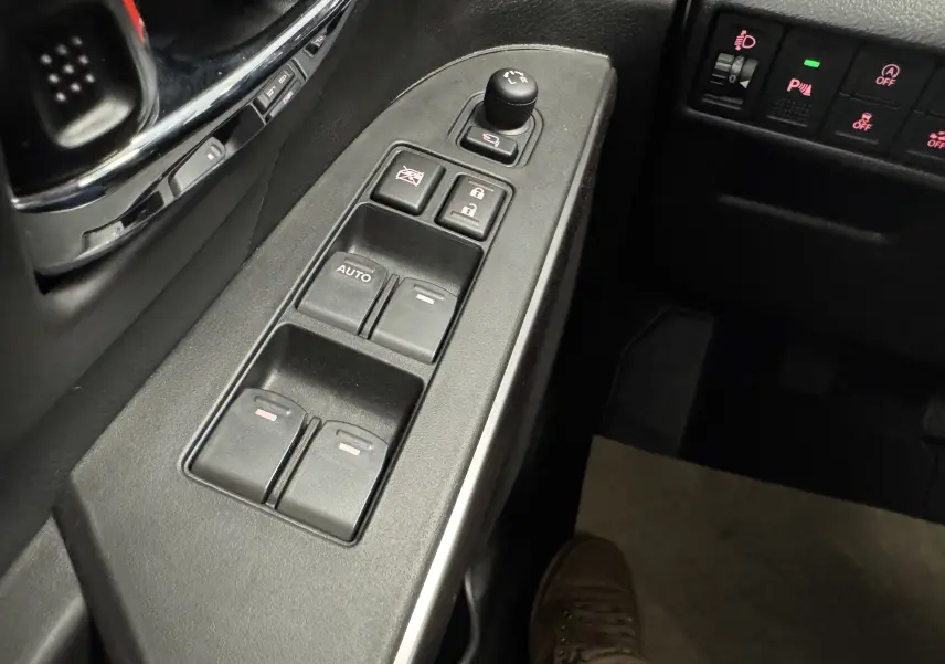 Gros plan sur les commandes des vitres et rétroviseurs côté conducteur du Suzuki S-Cross blanc 2025 hybride.