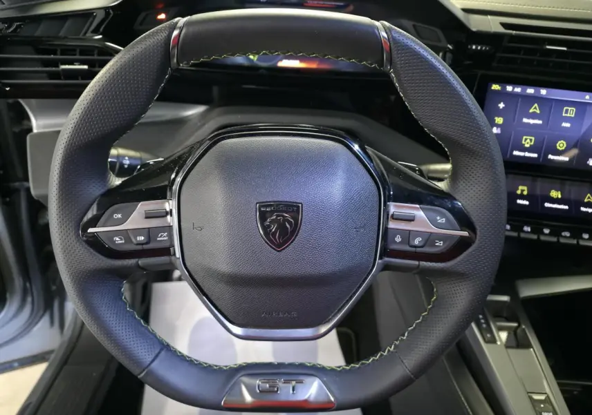 Volant cuir perforé noir avec surpiqûres vertes et badge GT du Peugeot 408 1.6 PHEV, vue de face intérieure.