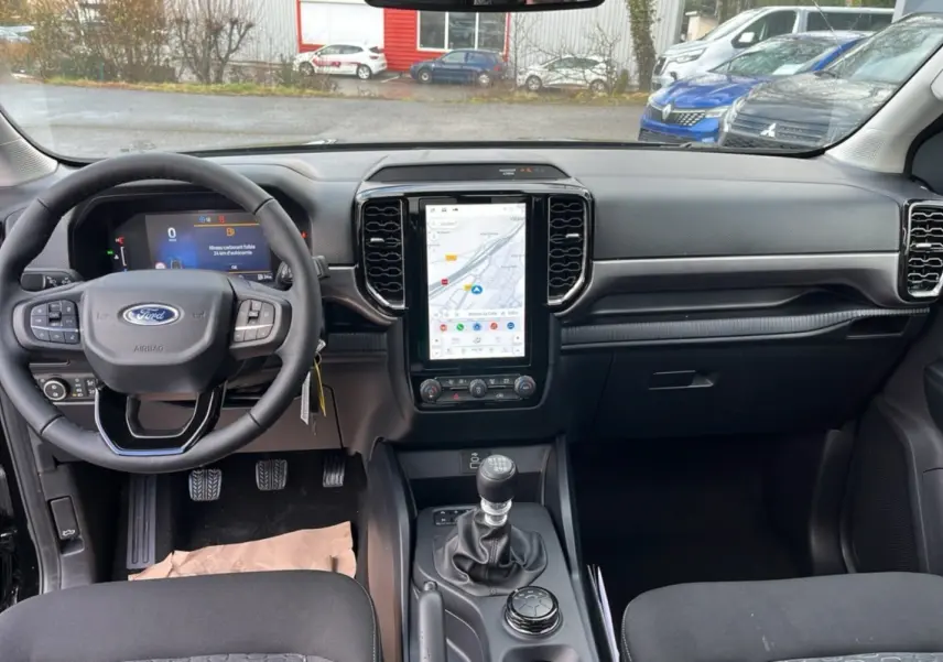 Vue intérieure avant du Ford Ranger noir shadow 2025, mettant en valeur le volant cuir multifonctions et l’écran tactile vertical.