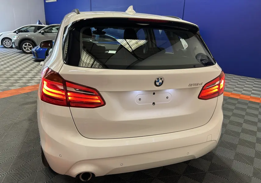 Vue arrière d'une BMW Série 2 Active Tourer 216d blanche avec feux arrière allumés dans un showroom.