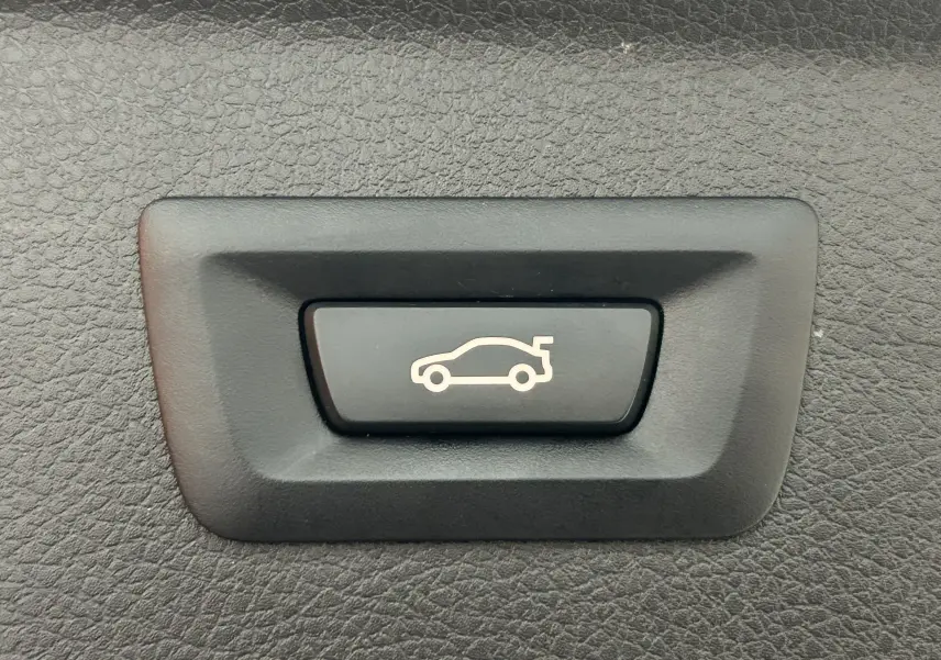 Bouton noir avec symbole blanc d'ouverture de coffre, sur panneau intérieur texturé noir d'une BMW Série 2 Active Tourer.