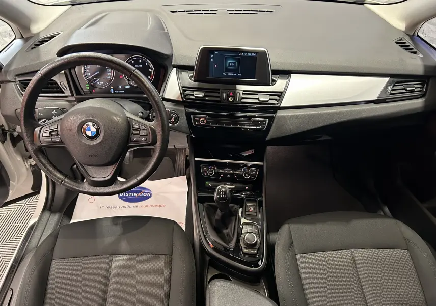 Vue intérieure avant de la BMW Série 2 Active Tourer 216d 2021, tableau de bord noir avec volant multifonction et console centrale manuelle.