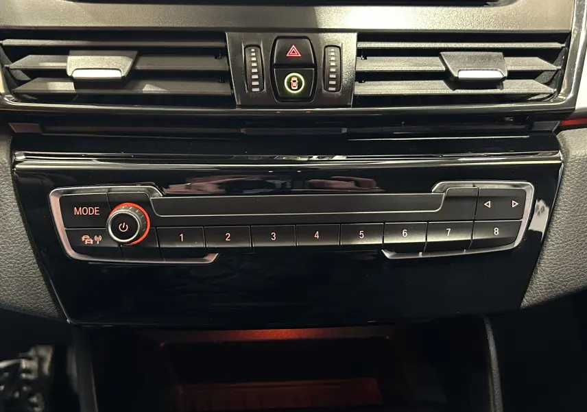 Vue rapprochée de la console centrale noire brillante avec commandes multimédia et ventilation d’une BMW Série 2 Active Tourer blanche.