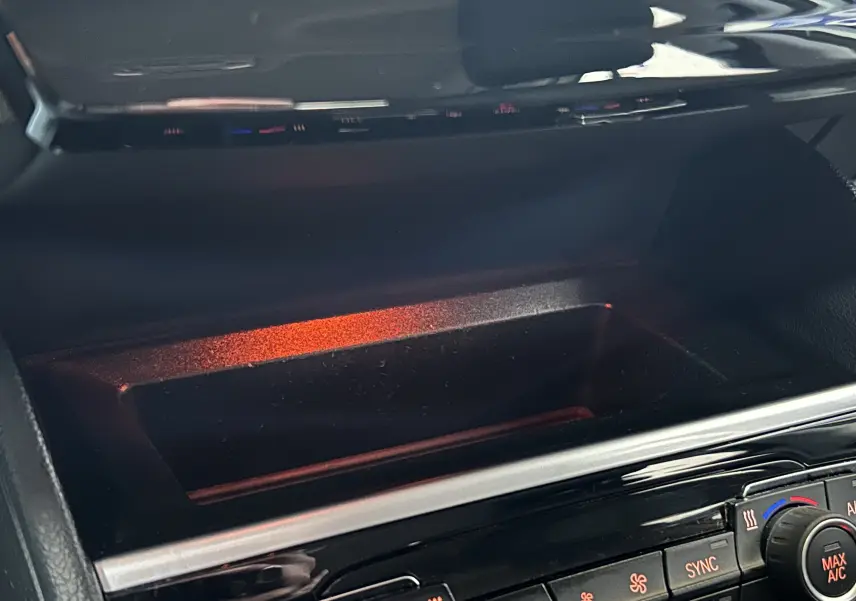 Gros plan sur la console centrale noire de la BMW Série 2 Active Tourer 216d, montrant les commandes de climatisation et un espace de rangement éclairé.
