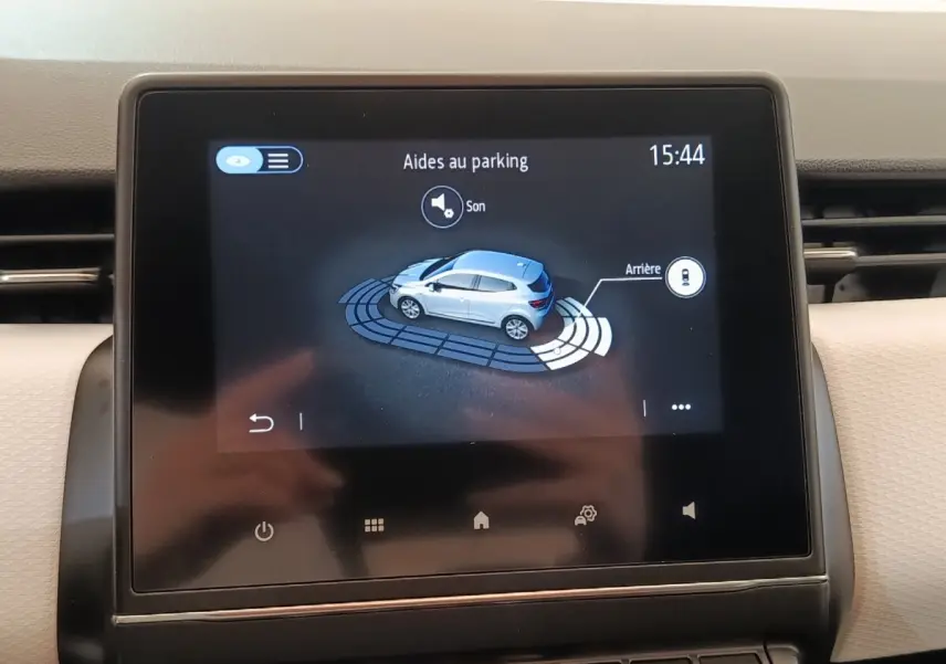 Écran tactile central affichant l'aide au stationnement de la Renault Clio blanche vue de dessus côté droit.