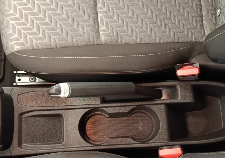 Vue plongeante sur la console centrale noire de la Renault Clio avec frein à main manuel et porte-gobelets.