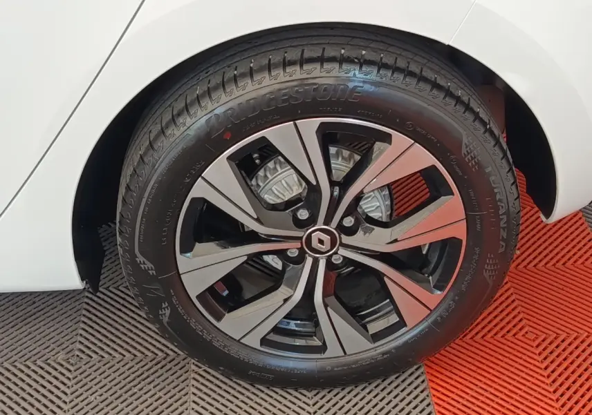 Gros plan sur la roue avant gauche d'une Renault Clio blanche, mettant en valeur la jante alliage au design moderne.