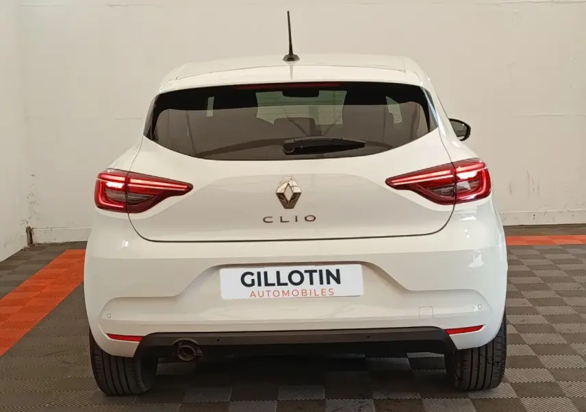 Vue arrière d'une Renault Clio blanche 2023 avec feux LED allumés et logo Renault visible au centre.