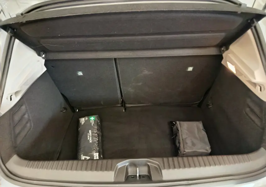Coffre ouvert de Renault Clio blanc, vue de l'arrière montrant un espace de rangement avec trousse de secours et sac noir.