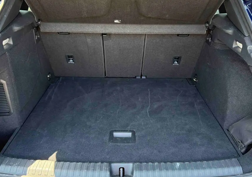 Coffre ouvert vu de l'arrière d'une CUPRA Terramar bleu, espace de chargement avec tapis noir et habillage intérieur sombre.