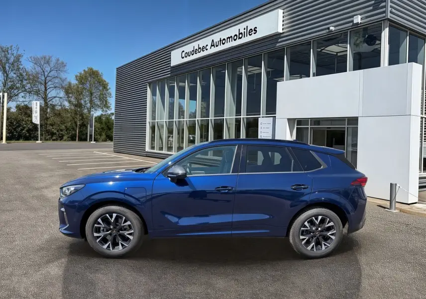 Vue de profil côté gauche d'un CUPRA Terramar bleu métallisé garé devant un bâtiment moderne de concession.