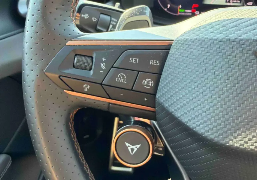 Gros plan sur le volant perforé noir avec logo CUPRA cuivré et commandes multifonctions côté gauche.