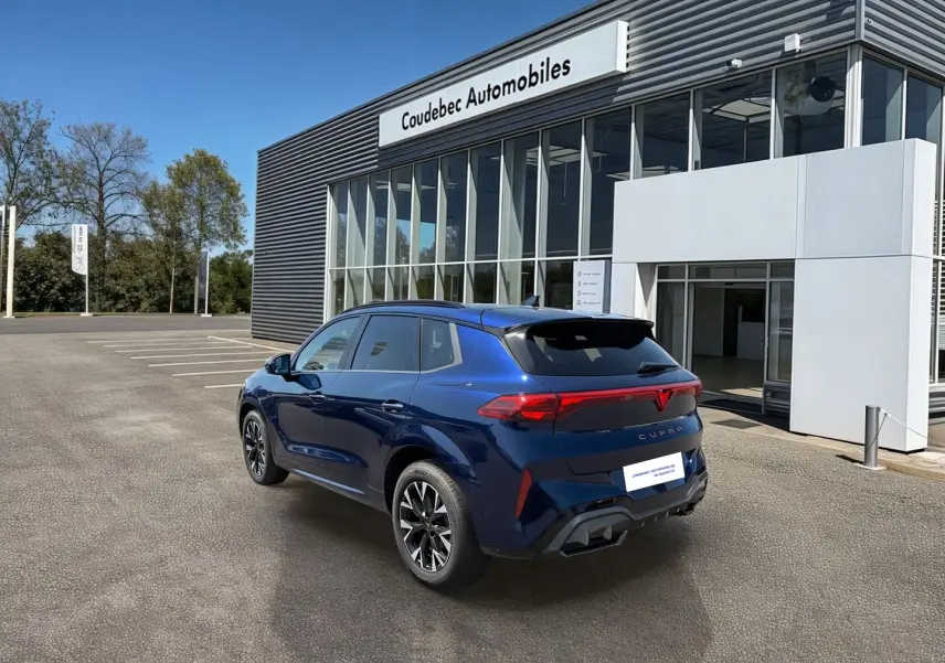 Vue 3/4 arrière droite d'un CUPRA Terramar bleu métallisé devant un bâtiment moderne avec logo CUPRA lumineux à l'arrière.