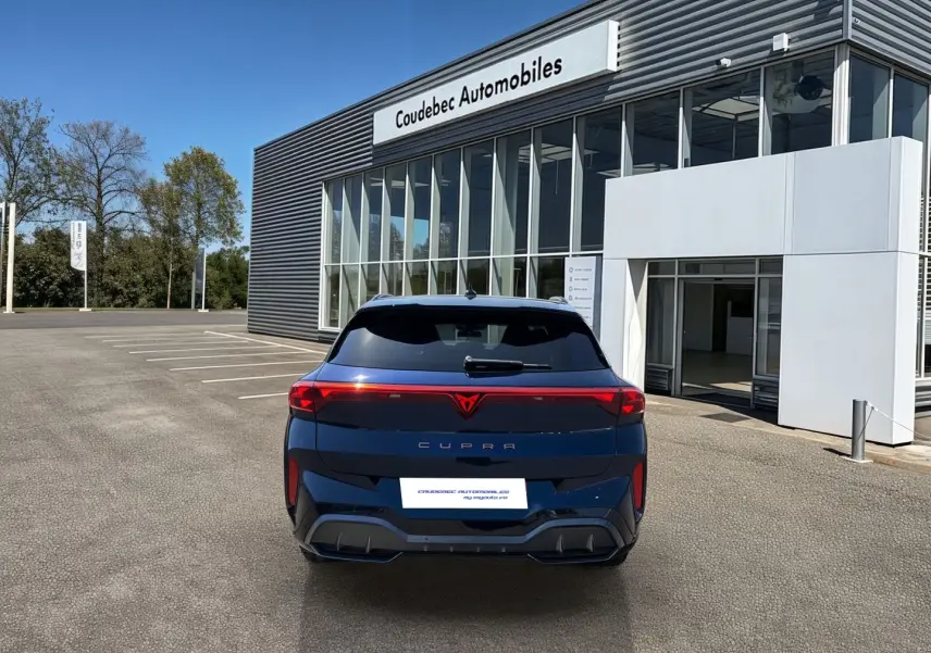 Vue arrière d'une CUPRA Terramar 2025 bleu cosmos avec bandeau lumineux et logo CUPRA rouge, stationnée devant un concessionnaire.