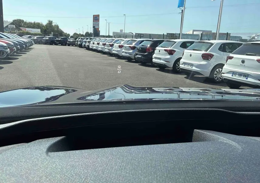 Vue depuis l’habitacle d’un CUPRA Terramar bleu, montrant le capot et un parking de voitures blanches à l’extérieur.