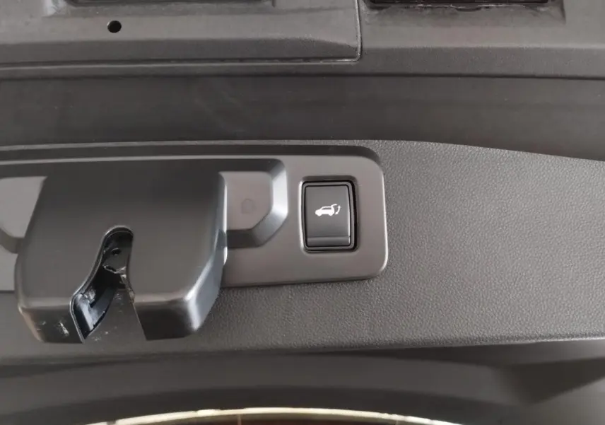 Gros plan sur le bouton d'ouverture électrique du hayon du Renault Symbioz gris Cassiopée, intérieur coffre.
