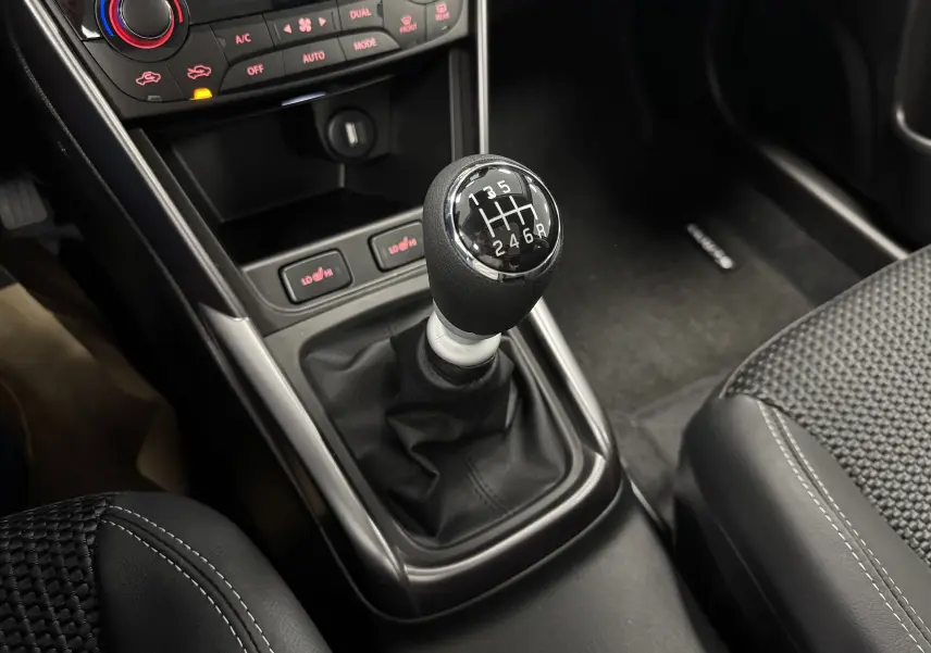 Gros plan sur le levier de vitesses manuel noir et argenté du Suzuki S-Cross 2025, avec console centrale et sièges en tissu gris.